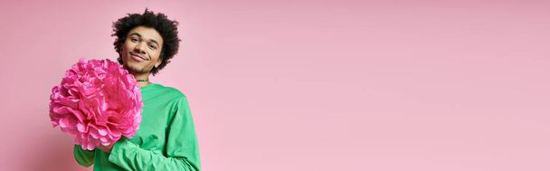 Allegro uomo afroamericano dai capelli ricci, in camicia verde, regge un delicato fiore rosa su uno sfondo rosa vivace. - Foto, immagini