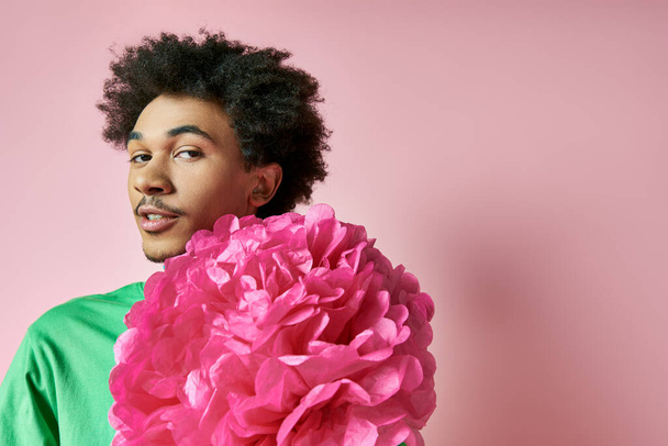 カジュアルな服装を着た陽気な若いアフリカ系アメリカ人男性が顔の前に大きなピンクの花を持ち,感情と優雅さを示しています.. - 写真・画像