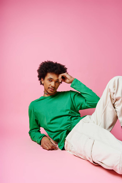 Hombre afroamericano alegre con pelo rizado en camisa verde casual y pantalones blancos, expresando emociones sobre fondo rosa. - Foto, Imagen