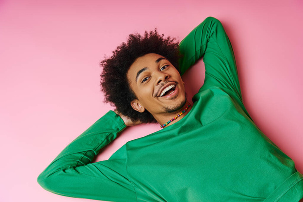 Χαρούμενος Αφροαμερικανός άνδρας με σγουρά μαλλιά ξαπλωμένος σε ένα ζωντανό ροζ φόντο, επιδεικνύοντας μια αίσθηση ικανοποίησης. - Φωτογραφία, εικόνα