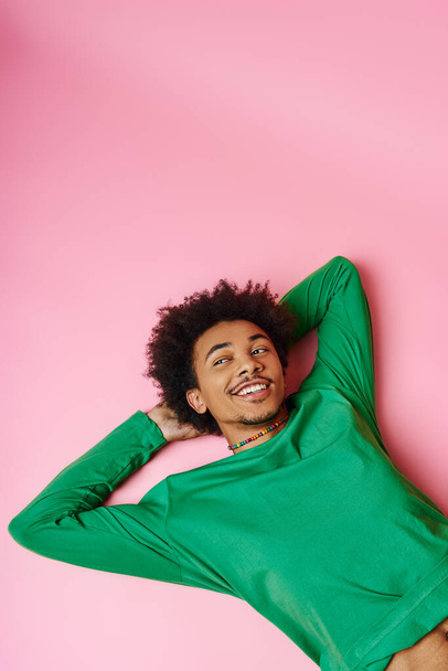 A cheerful curly African American man in a green shirt laying peacefully on a vivid pink background. - Photo, Image
