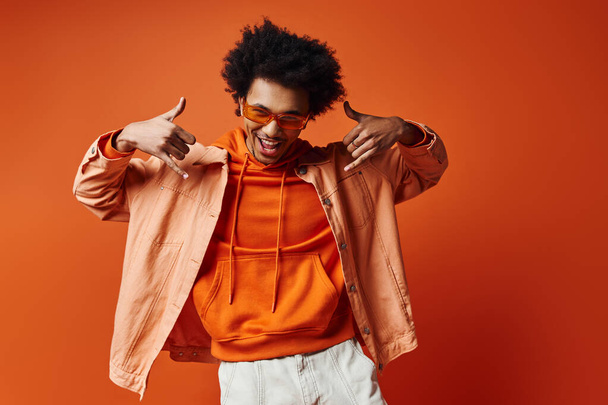 Стильный молодой афроамериканец с вьющимися волосами в толстовке и белых шортах на оранжевом фоне. - Фото, изображение