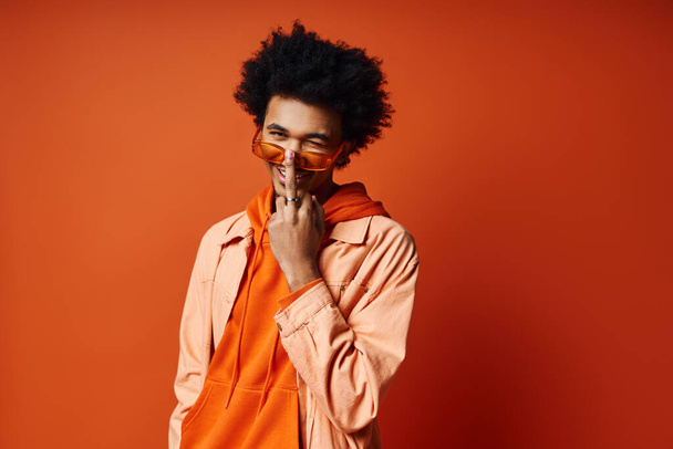 Elegante giovane uomo afroamericano, capelli ricci, camicia arancione, mani sul viso, esprimendo emozione, sfondo alla moda. - Foto, immagini