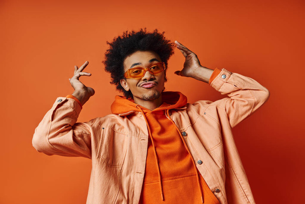 Stylish African American man in orange jacket and glasses against a bold orange background. - Photo, Image
