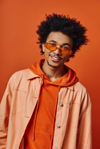 Turuncu arka planda turuncu gömlek ve ceket giyen kıvırcık saçlı, şık, Afro-Amerikan bir adam, çeşitli duygular gösteriyor.. - Fotoğraf, Görsel