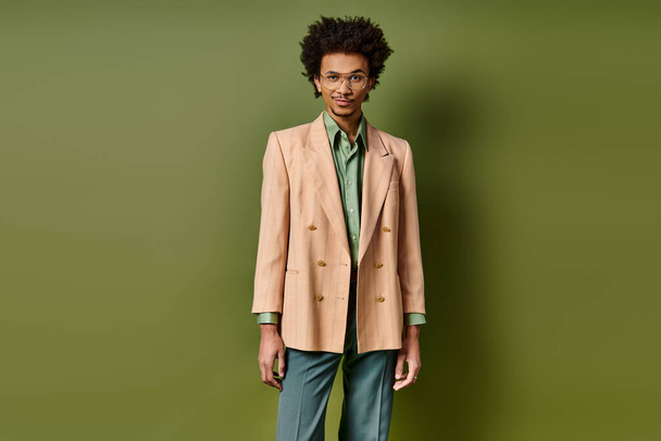 Κομψός νεαρός, σγουρός Αφροαμερικανός με κοστούμι που στέκεται με αυτοπεποίθηση μπροστά σε έναν ζωντανό πράσινο τοίχο.. - Φωτογραφία, εικόνα