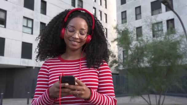 Gyönyörű fekete nő fülhallgatóval zenét hallgat. Boldog online vásárlást mobiltelefonnal az egyszerű és biztonságos távoli elektronikus fizetésekhez.  - Felvétel, videó