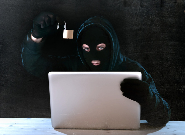 gevaarlijke hacker man met computer en lock hacking systeem in cyber misdaad concept - Foto, afbeelding