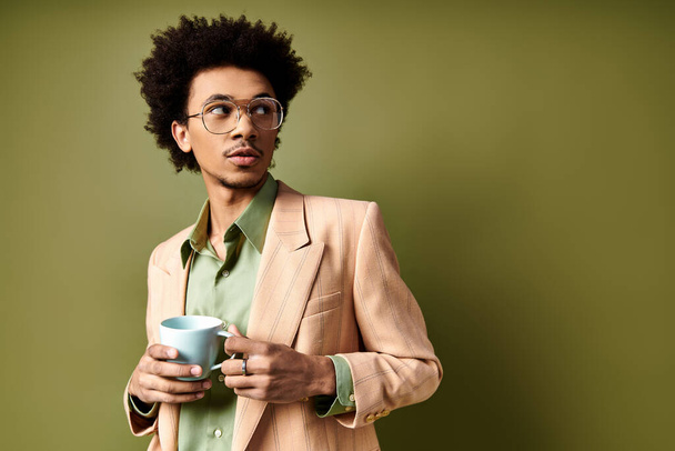 Stilvoller junger afroamerikanischer Mann in schickem Anzug und Sonnenbrille, der eine Tasse Kaffee vor grünem Hintergrund genießt. - Foto, Bild