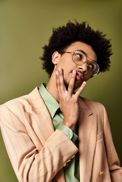 Tyylikäs, nuori, kihara afroamerikkalainen mies puvussa ja laseissa tekee hassut kasvot vihreää taustaa vasten.. - Valokuva, kuva