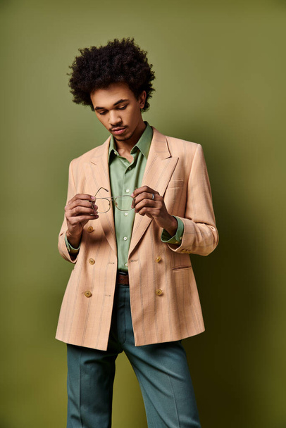 スタイリッシュな若いアフリカ系アメリカ人男性で,タンジャケット,緑のシャツ,活気に満ちた緑の背景にサングラスを着用しています.. - 写真・画像