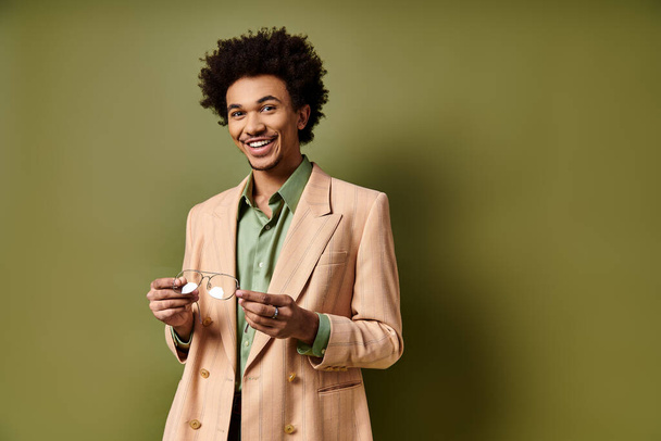 A stylish young African American man in a suit holding glasses against a vibrant green background. - Photo, Image