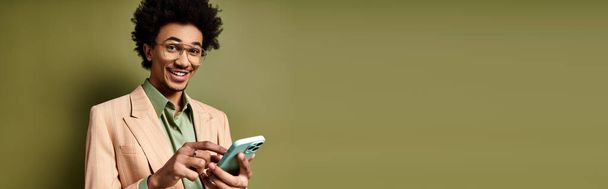 Стильний молодий афроамериканський чоловік у костюмі та сонцезахисних окулярах тримає мобільний телефон на зеленому тлі. - Фото, зображення