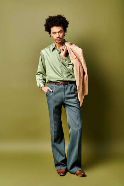 Elegante giovane uomo afro-americano con i capelli ricci indossa una camicia verde e pantaloni blu, occhiali da sole sportivi su uno sfondo verde. - Foto, immagini