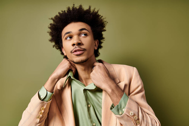 Un giovane afroamericano elegante con i capelli ricci, indossando una giacca tuta e una camicia verde, posa con fiducia su uno sfondo verde. - Foto, immagini
