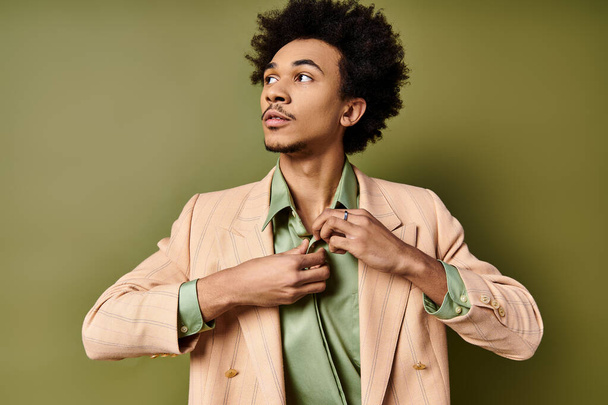 スーツのスタイリッシュな若いアフリカ系アメリカ人男性は,緑色の背景の前でシャツを巧みにボタン化しています. - 写真・画像