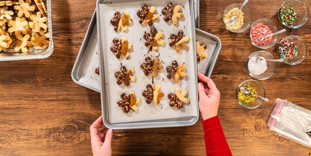 Δημιουργία μπισκότων ζάχαρης σε σχήμα νιφάδας, βουτηγμένα σε σοκολάτα και στολισμένα με θρυμματισμένα καρύδια πεκάν, κομψά τοποθετημένα σε περγαμηνή. - Φωτογραφία, εικόνα