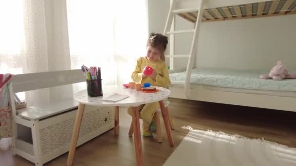 Bambina giocare con la cucina giocattolo di plastica al chiuso a casa. La bambina beve il tè da una tazza giocattolo - Filmati, video