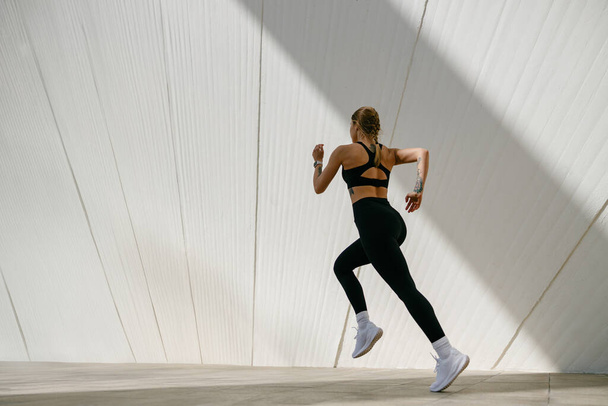 Młoda kobieta w odzieży sportowej biegnie na tle nowoczesnych budynków. Koncepcja aktywnego stylu życia - Zdjęcie, obraz