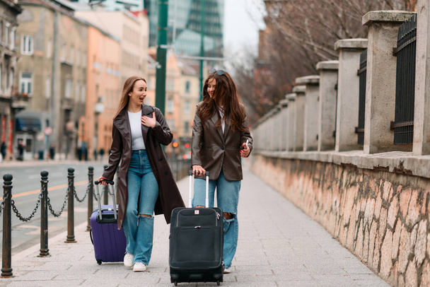 Deux touristes féminines explorent une ville européenne, traînant leurs valises dans les rues charmantes, s'immergeant dans la culture et la beauté de leur destination de voyage. - Photo, image