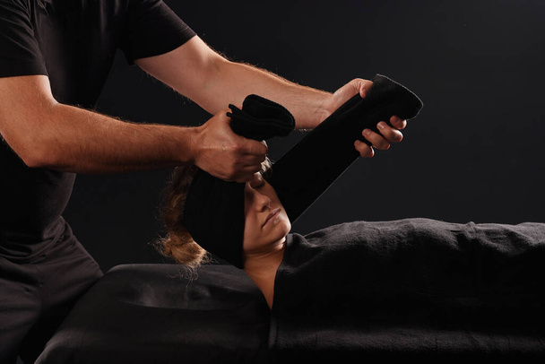 Ein professioneller Masseur oder Massagetherapeut wickelt ein Handtuch um den Hals eines Klienten und führt eine Nackendehnung durch. der Kunde liegt auf dem Massagetisch, der mit einem Handtuch bedeckt ist - Foto, Bild