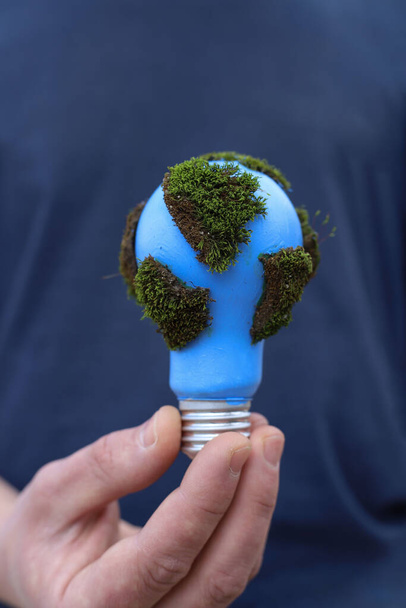 Soziale Probleme. Tag der Erde. eine blaue Glühbirne mit grünem Moos ist in den Händen eines Mannes geschützt - Foto, Bild
