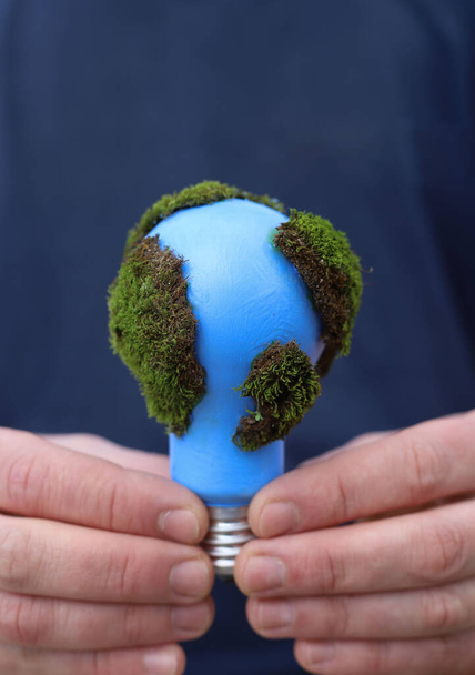 Soziale Probleme. Tag der Erde. eine blaue Glühbirne mit grünem Moos ist in den Händen eines Mannes geschützt - Foto, Bild
