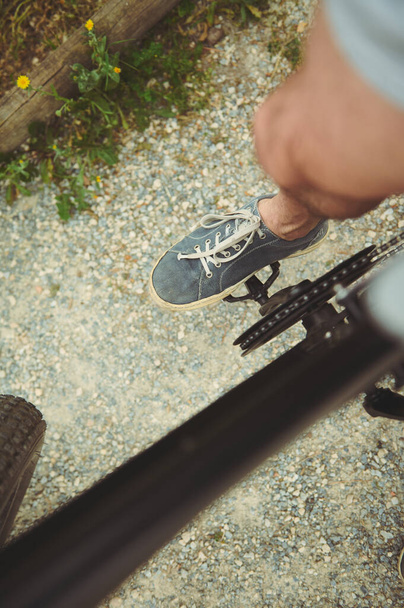 Cyclist point of view. Close-up view from above of male foot in denim sneakers on the electric bike pedal, riding outdoors - Photo, Image