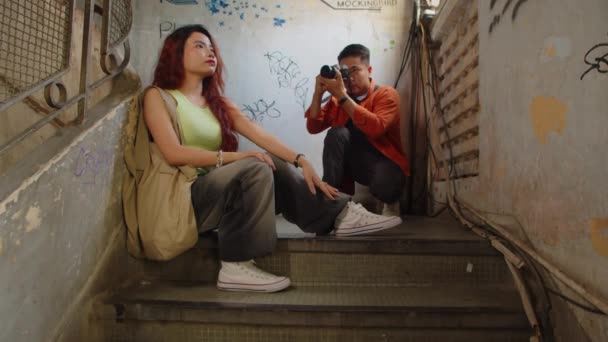 Largo tiro de la joven modelo sentada en las escaleras y posando para el fotógrafo dentro del edificio abandonado - Imágenes, Vídeo