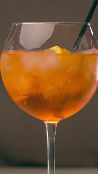 Bicchiere di Aperol Spritz cocktail su sfondo grigio. Miscelare Aperol Spritz con una cannuccia da cocktail. Video verticale - Filmati, video