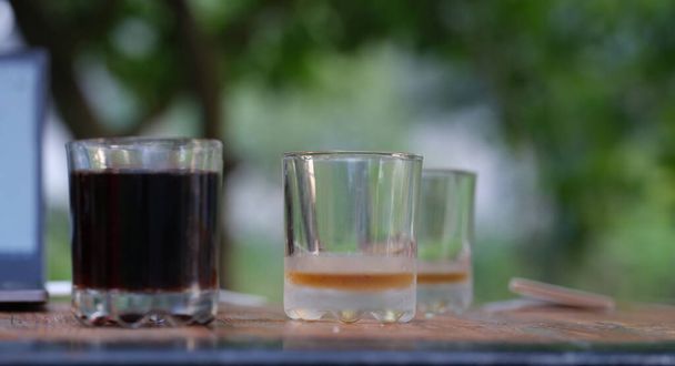 İki şeffaf cam bardak koyu sıvı ve boş ayakta duruyor. Yaz kafeleri konseptinde içki içmek. - Fotoğraf, Görsel