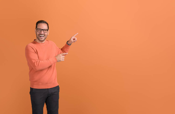 Retrato del promotor masculino riendo y apuntando al espacio de la copia mientras que la comercialización en fondo naranja - Foto, Imagen