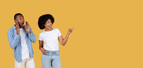 Wyraźna młoda para Afroamerykanów, wskazująca i reagująca z zaskoczeniem i podnieceniem na żółtym tle - Zdjęcie, obraz