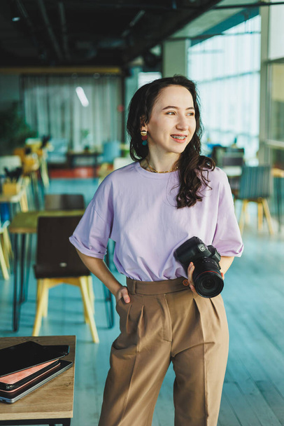 Μια νεαρή ανεξάρτητη φωτογράφος δουλεύει σε ένα λάπτοπ σε μια καφετέρια. Γυναίκα φωτογράφος ρετουσάρει φωτογραφίες σε ένα φορητό υπολογιστή - Φωτογραφία, εικόνα