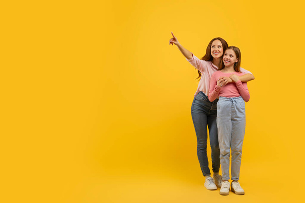Gülümseyen ikili, anne ve genç kız yukarıdaki bir şeyi işaret ediyor sarı arkaplanda heyecanla, boşluğu kopyala - Fotoğraf, Görsel