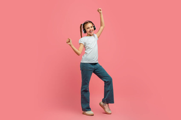 A lány élvezi a zenét fejhallgatóval tánc közben, mutatja dinamikus mozgás rózsaszín háttér, teljes hossz - Fotó, kép