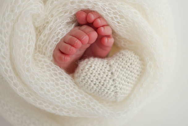 The tiny foot of a newborn baby. Soft feet of a new born in a white wool blanket. Close up of toes, heels and feet of a newborn. Knitted white heart in the legs of a baby. Macro photography  - Photo, Image