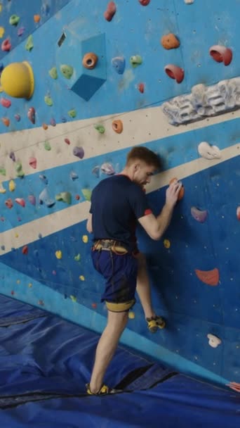 Verticaal schot van sterke man in sportkleding klimwand zonder belay tijdens het beoefenen van boulderen in de sportschool - Video