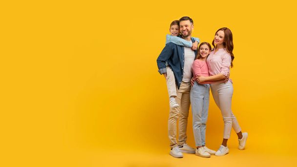 Close-knit familie bundel samen, het weergeven van genegenheid en glimlacht op een zonnige studio gele achtergrond - Foto, afbeelding