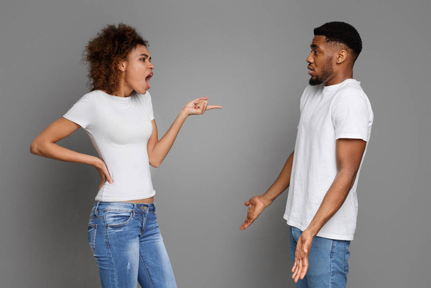 Emocional chica afroamericana gritándole a su novio confundido, fondo gris estudio
. - Foto, imagen