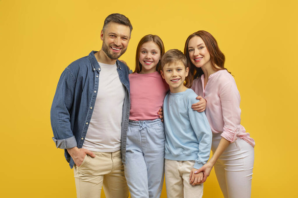 Veselá rodina se dvěma dětmi stojí spolu, ukazuje jednotu rodiny na žlutém pozadí - Fotografie, Obrázek