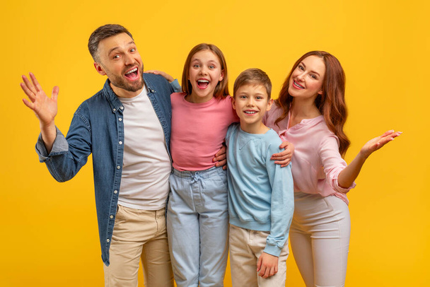 Παιχνιδιάρικη οικογένεια με υπερβολικά χαρούμενες εκφράσεις σε ένα φωτεινό κίτρινο φόντο για ένα διασκεδαστικό πορτρέτο - Φωτογραφία, εικόνα