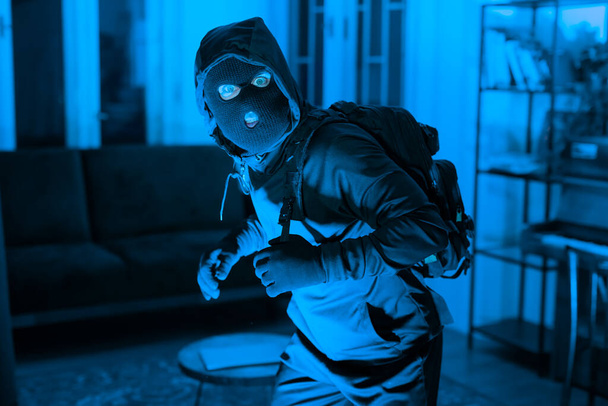 Нарушитель на цыпочках с осторожностью проходит через темную атмосферу комнаты, изображая напряженность и неминуемую угрозу обнаружения - Фото, изображение