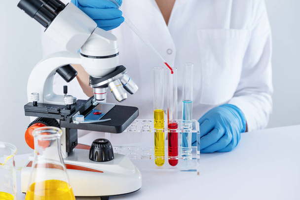 Biotechnologin arbeitet im Labor mit chemischer Flüssigkeit. Wissenschaftler forschen im Labor, im Reagenzglas mit Flüssigkeit und unter dem Mikroskop. Blut fällt von der Pipette in die Blutentnahmeröhre. - Foto, Bild