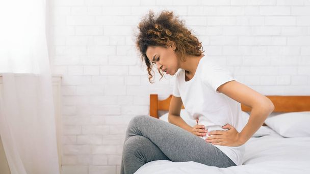 Δυστυχισμένη γυναίκα που πάσχει από στομαχόπονο, κάθεται στο κρεβάτι το πρωί - Φωτογραφία, εικόνα