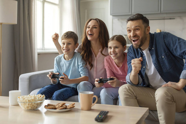 Emocionado padre de familia madre e hijos disfrutando de una sesión de juego en su sofá con alegría y risa juntos - Foto, Imagen