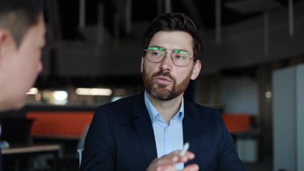 Egy fehér férfi arcképe szemüvegben, üzleti ruhában és tollal a kezében gesztikulálva. A növekedési stratégia adatainak a befektetőkkel való együttműködés mellett történő megosztásával foglalkozó ügyvezető igazgató. - Felvétel, videó