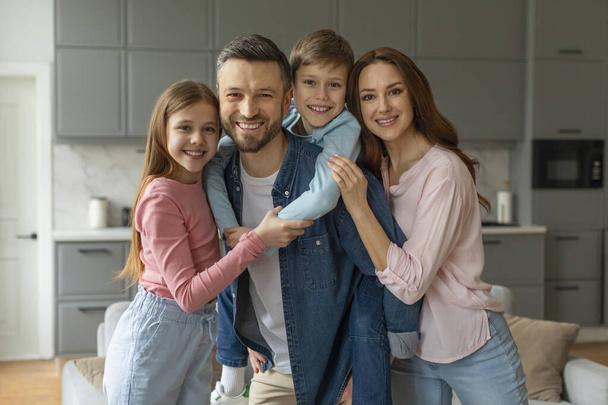 Eine fröhlich liebende europäische Familie mit zwei Kindern, die lächelnd und umarmend in einem gemütlichen, modernen Zuhause leben - Foto, Bild