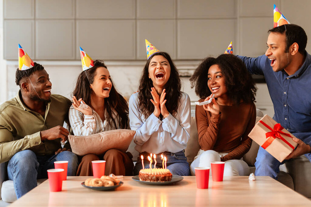 A diverse group of multiracial friends laughs and enjoys a birthday party together, with cake and candles on the table - Photo, Image