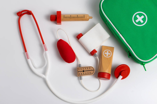 kit de juguetes de primeros auxilios para niños sobre fondo blanco, bolsa verde con herramientas médicas - Foto, Imagen
